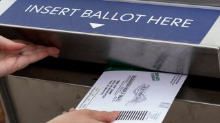 FILE – A Michigan voter inserts her absentee voter ballot into a drop box in Troy, Mich. on Oct. 15, 2020.