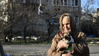 Local resident Galyna, 80, holds a cat in front of a damaged building where she lives without electricity, water and heat, in the town of Lyman, Donetsk region, on December 14, 2022, amid the Russian invasion of Ukraine.