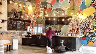 Alloyius Mcilwaine at work on the giant 25-foot-tall mural that will be displayed inside the Brewerytown Food Hall.