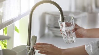 Woman pouring water into glass in kitchen, closeup