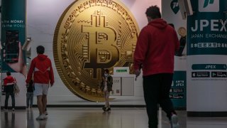 Pedestrians walk past an advertisement displaying a Bitcoin cryptocurrency token on February 15, 2022 in Hong Kong, China.