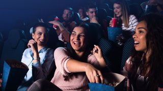 Group of cheerful people laughing while watching movie in cinema.