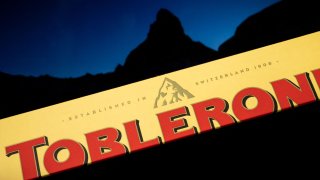 A picture taken on March 6, 2023 in Geneva shows a the packaging of a Toblerone chocolate bar owned by US firm Mondelez with a picture of the Matterhorn mountain seen in silhouette in the background. – Toblerone is to remove the Swiss iconic Matterhorn peak from its packaging when some of the chocolate’s production is moved from Switzerland to Slovakia and replaced by a more generic mountain under strict “Swissness” rules.