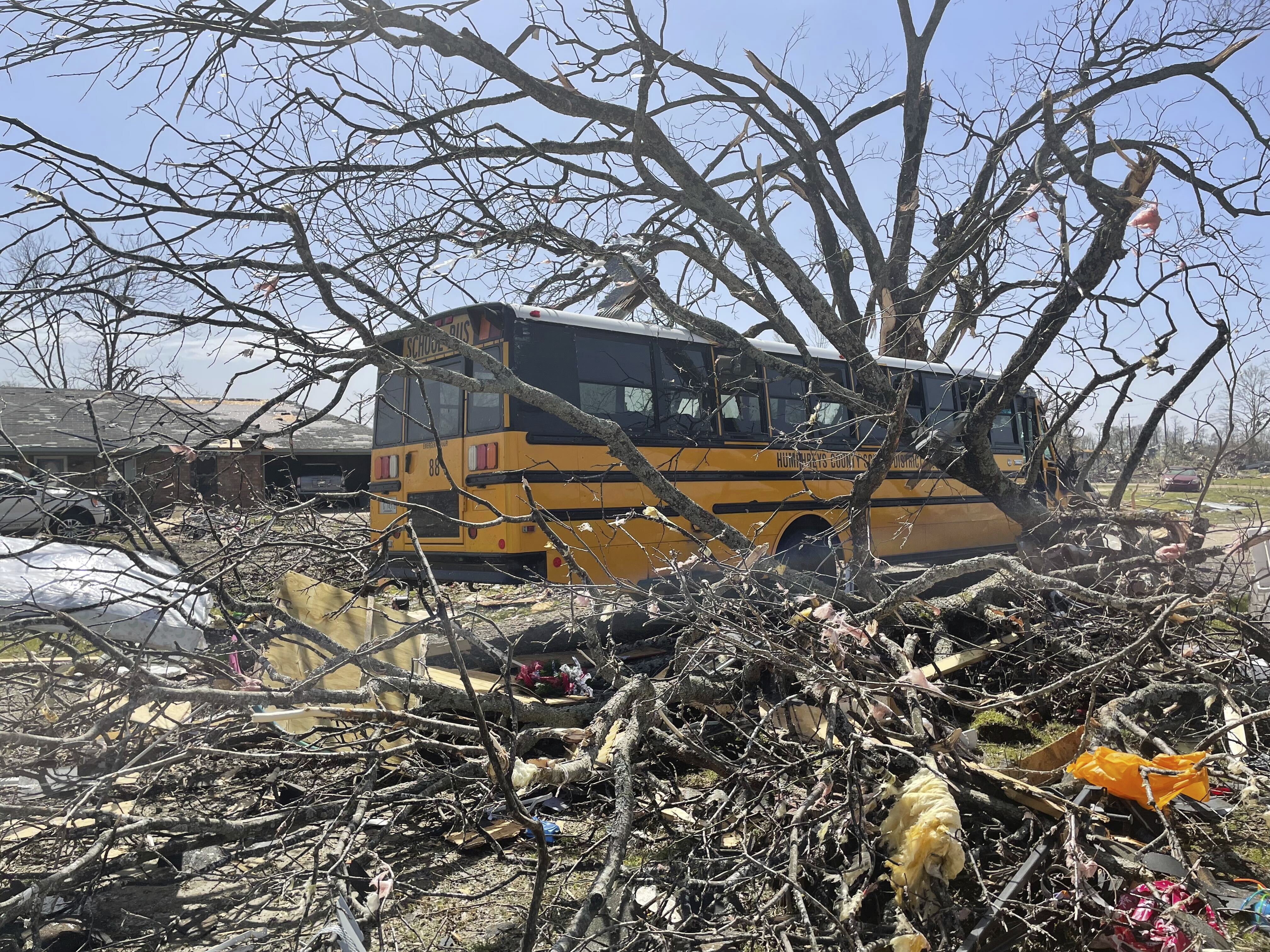 A bus passes debris on Saturday, March 25, 2023 in Silver City, Miss.  Emergency officials in Mississippi say several people have been killed by tornadoes that tore through the state on Friday night, destroying buildings and knocking out power as severe weather produced hail the size of golf balls moved through several southern states.  (AP Photo/Michael Goldberg)