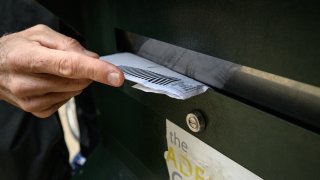 Hand putting ballot into mail slot.