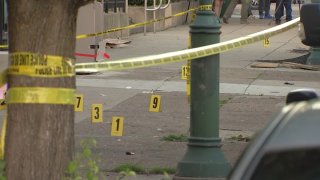 Police tape in front of a sidewalk with yellow crime markers on the ground.