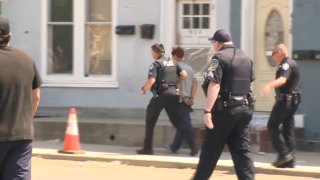 Police lead a person in handcuffs down a sidewalk.