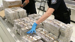 An officer at the Philadelphia International Airport leans over a pile of millions of bills of counterfeit cash.