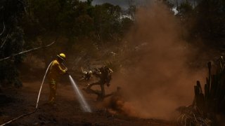 A Maui County firefighter uses a hose line to extinguish a fire near homes