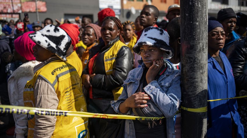 People watch on as firefighters work at the scene of a burned out apartment block in Johannesburg on August 31, 2023.