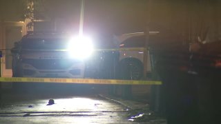 Police car shines light toward yellow crime scene tape