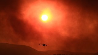 TOPSHOT – A helicopter flies over as wildfire rages near Alexandroupoli, northern Greece, on August 21, 2023. The European Union announced it was deploying two Cyprus-based fire-fighting aircraft and a Romanian fire-fighting team via the bloc’s civil protection mechanism, as wildfires rage uncontrolled in Greece for a third day. (Photo by Sakis MITROLIDIS / AFP) (Photo by SAKIS MITROLIDIS/AFP via Getty Images)