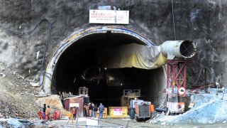 People stand near the entrance to the site of an under-construction road tunnel that collapsed in mountainous Uttarakhand state, India