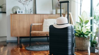 Still life of a black suitcase with a straw hat in the living room of an apartment. Travel and vacation concept