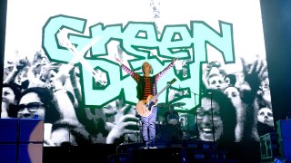 Billie Joe Armstrong with arms outstretched in front of "Green Day" written on a screen.