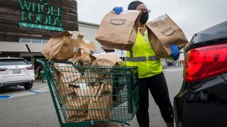 An independent contractor wearing a protective mask and gloves loads Amazon Prime grocery bags into a car outside a Whole Foods Market in Berkeley, California, on Oct. 7, 2020.