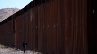 A man walks along the steel columns of the border wall separating Arizona and Mexico