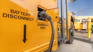 Yellow electric school bus plugged in at a charging station.