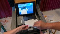 A polling judge, right, helps guide a voter's ballot into a voting machine during the Pennsylvania primary election, at Mont Alto United Methodist Church in Alto, Pa., on May 17, 2022.