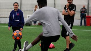 Carli Lloyd, left, watches Nur, a migrant from Somalia ,as he kicks the ball at Olympiacos Training Center in Athens, Monday, April 22, 2024.