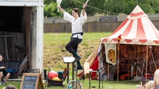 A person riding on a unicycle juggling at the Philadelphia Renaissance Faire.