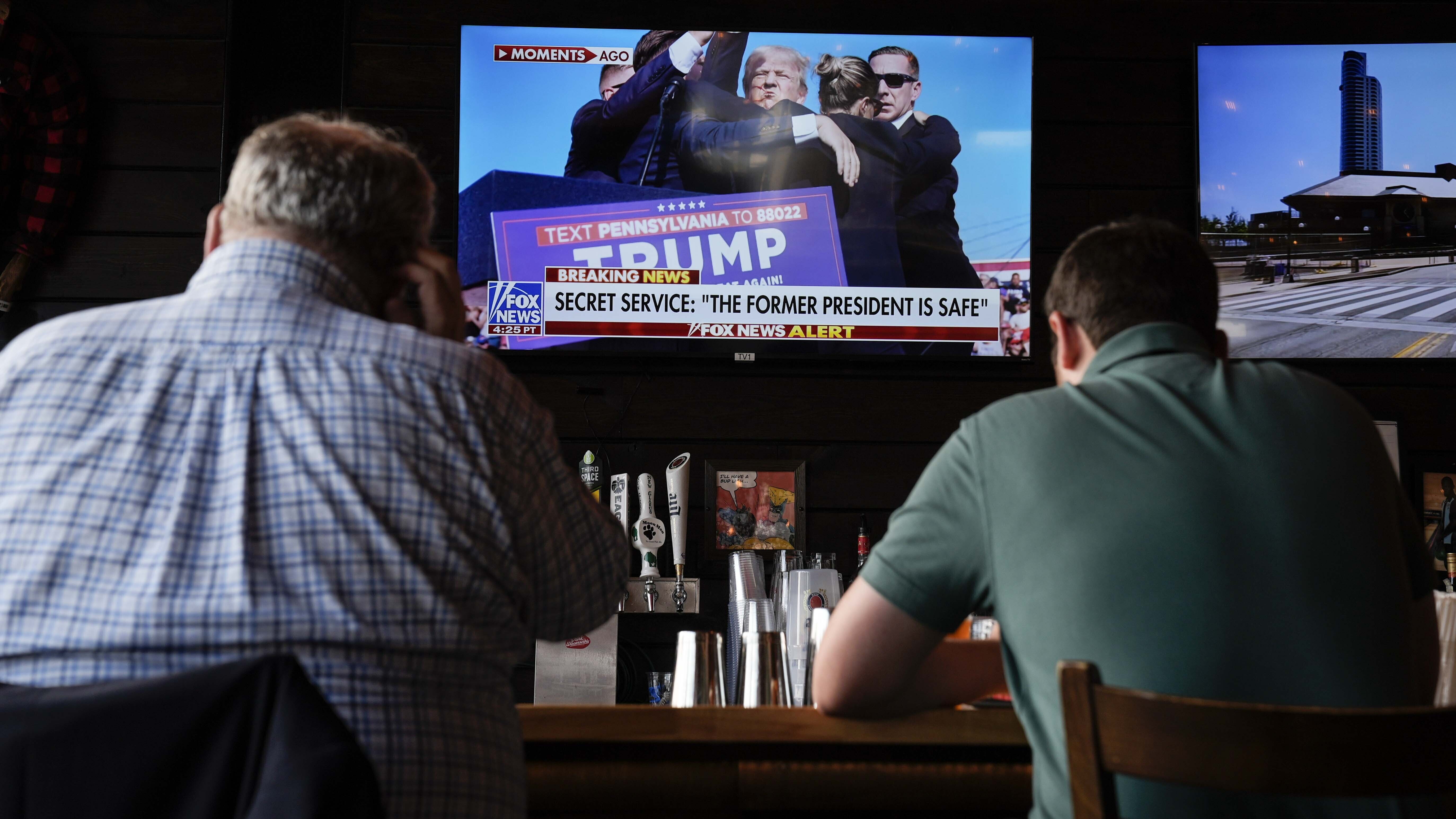 People sit in a local bar near the Fiserv Forum watching news