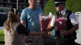 A police officer receives flowers to lay at the scene of a multiple stabbing attack on July 29, 2024 in Southport, England. The North West Ambulance Service says they were treating at least eight people for stab injuries after a reported attack near Hart Street.