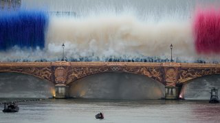 The Olympic torch travels by boat as ceremonial smoke in the colors of the France flag appear over the Seine River Paris, France, during the opening ceremony of the 2024 Summer Olympics, Friday, July 26, 2024.