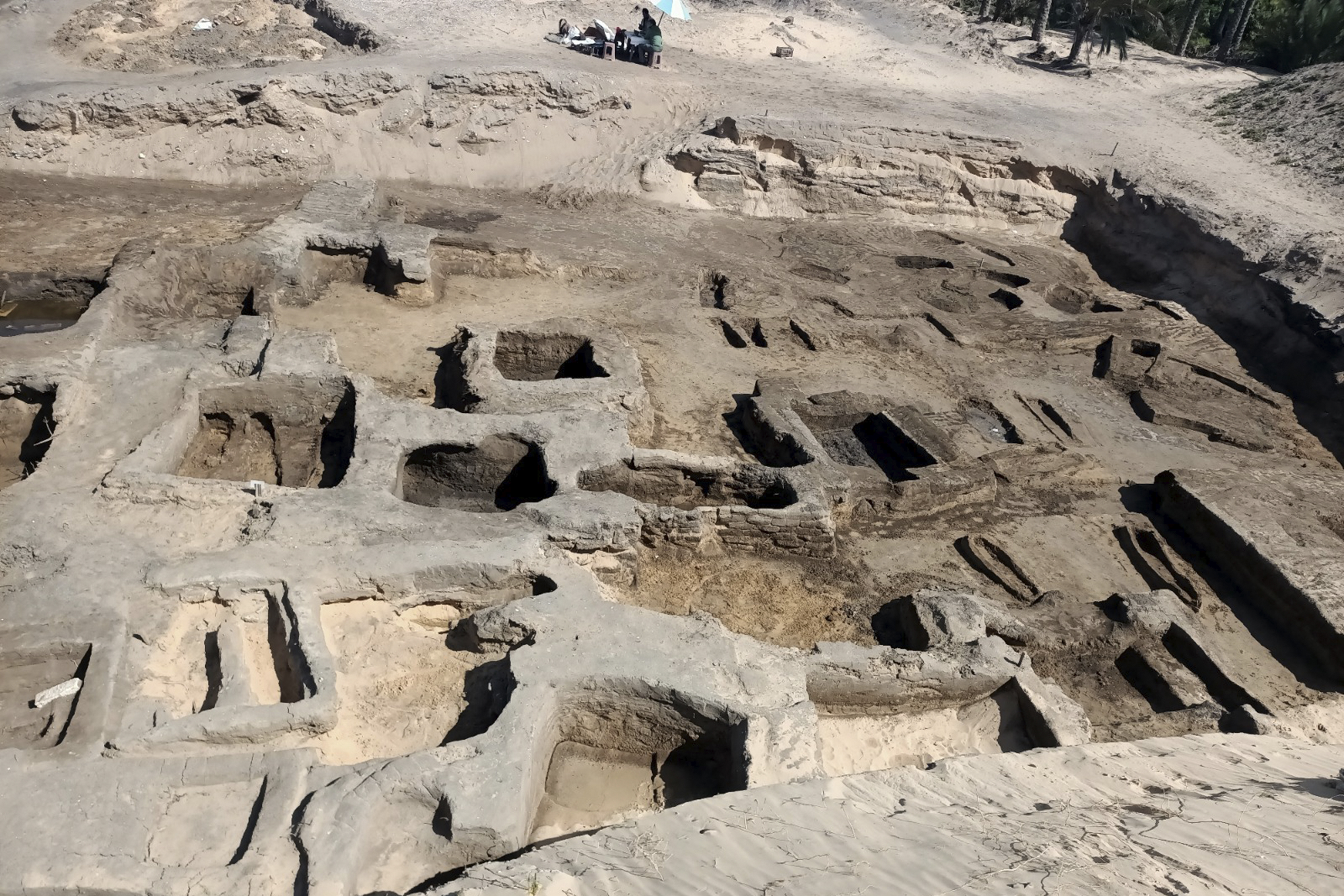 In this image provided by Egypt's Supreme Council of Antiquities, archeologists observe the site where they discovered 63 mud-brick tombs at the Tell al-Deir necropolis, in the Nile Delta town of Damietta, about 125 miles (200 km) north of Cairo, Egypt. The Egyptian Ministry of Tourism and Antiquities announced the discovery of the trove, which includes gold pieces, bronze coins and amulets on July 25, 2024. ( Egypt's Supreme Council of Antiquities via AP)