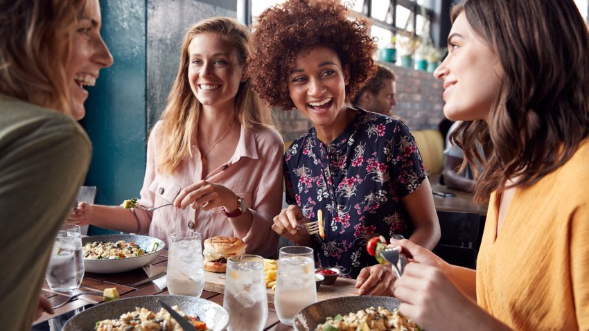 Four Young Female Friends Meeting For Drinks And Food Making A Toast In Restaurant