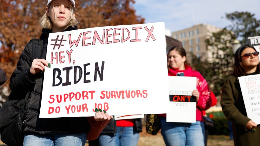 Activists hold up signs as they listen during a Title IX