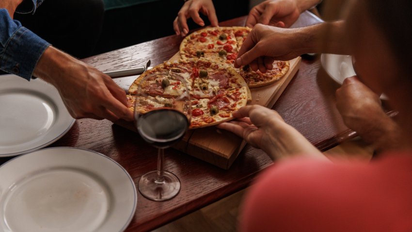 Group of friends hanging out in the living room, sharing and enjoying homemade pizzas and red wine.