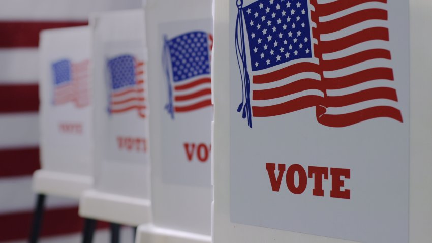 Straight on row of voting booths at polling station during American election. US flag in background.