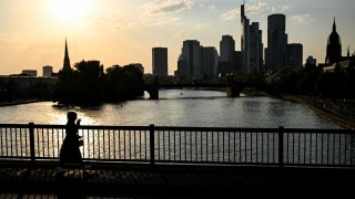 A woman walks on a bridge in front of the banking district skyline with the Commerzbank building (3R) and the Cathedral (R) during sunset in Frankfurt am Main, western Germany, on September 18, 2024.