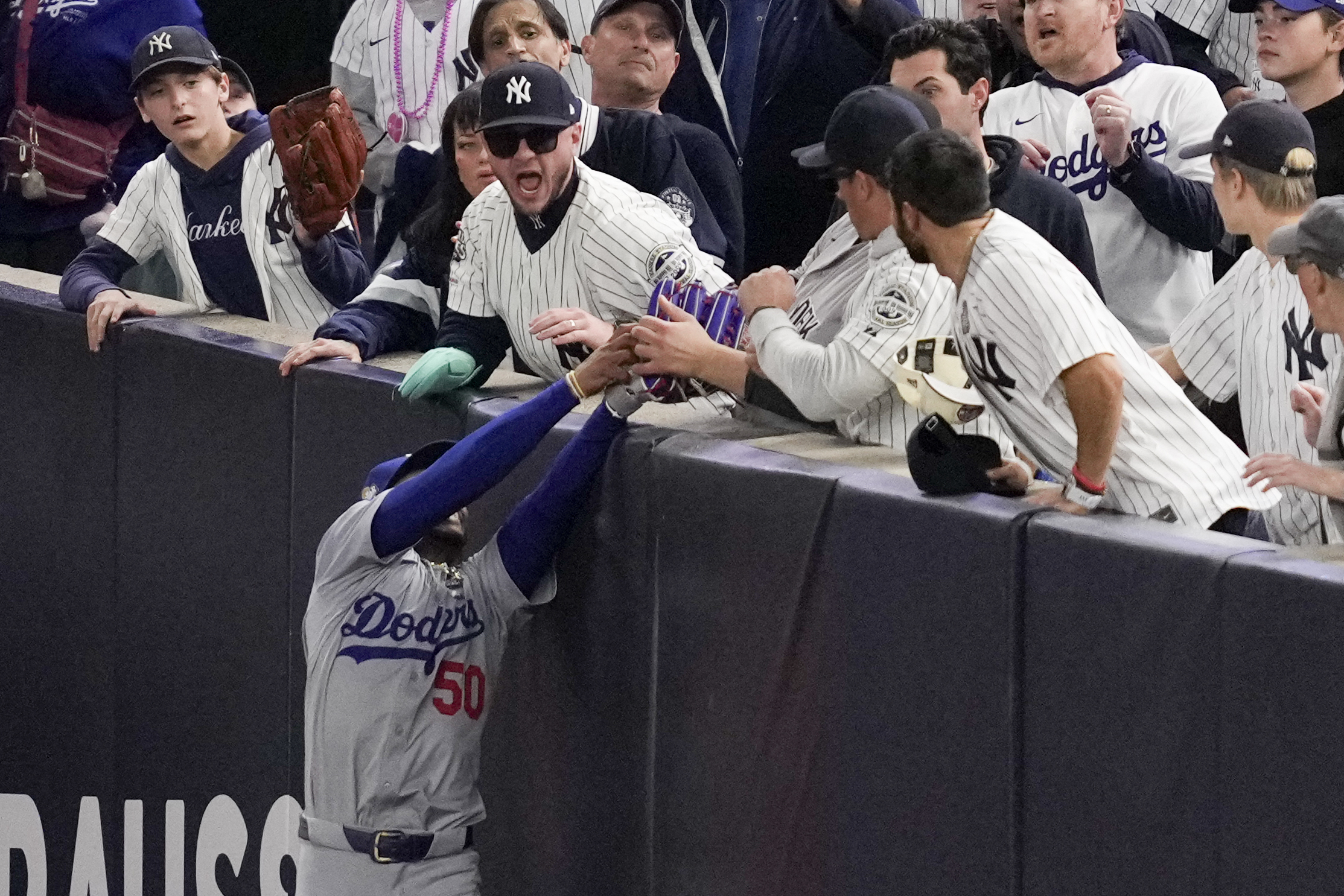 Fans interfere with a foul ball caught by Los Angeles Dodgers right fielder Mookie Betts during the first inning in Game 4 of the baseball World Series against the New York Yankees, Tuesday, Oct. 29, 2024, in New York. (AP Photo/Ashley Landis)