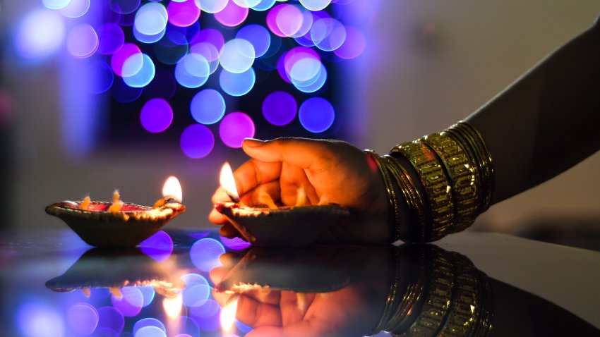 Female hand holding a Diwali lamp on the foreground of a beautifully illuminated background of colourful bokeh