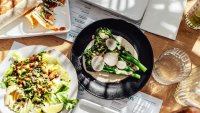 A plate of fresh leaf salad with avocado, grilled broccoli and burrito served on the table with bright sunlight