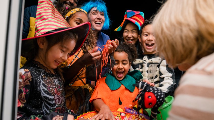 Taken from inside a residential house, two families wearing fancy dress, out trick or treating in North East England during halloween. The children are taking sweets off a plate that an unrecognisable woman is holding.