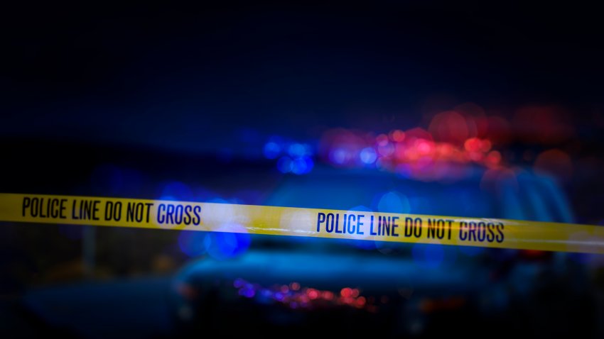 A stock photo of a Police Line "Do Not Cross" caution tape with a defocused police car with sirens flashing red and blue.