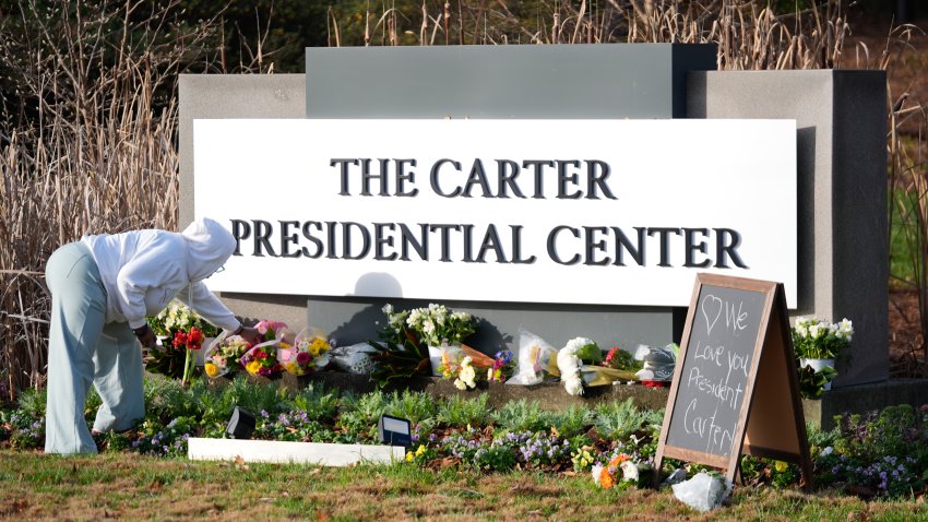 Christine Mason, of Atlanta, places flowers at entrance the The Jimmy Carter Presidential Center in Atlanta Monday, Dec. 30, 2024, in Atlanta. Formr President Jimmy Carter died Sunday at his home in Plains, Ga, at the age of 100.