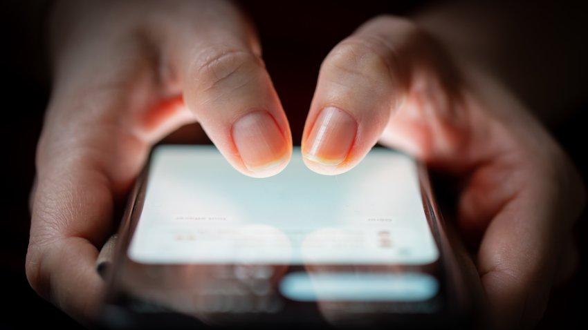 Close-up of two woman’s thumbs touching on a smartphone screen in the dark.