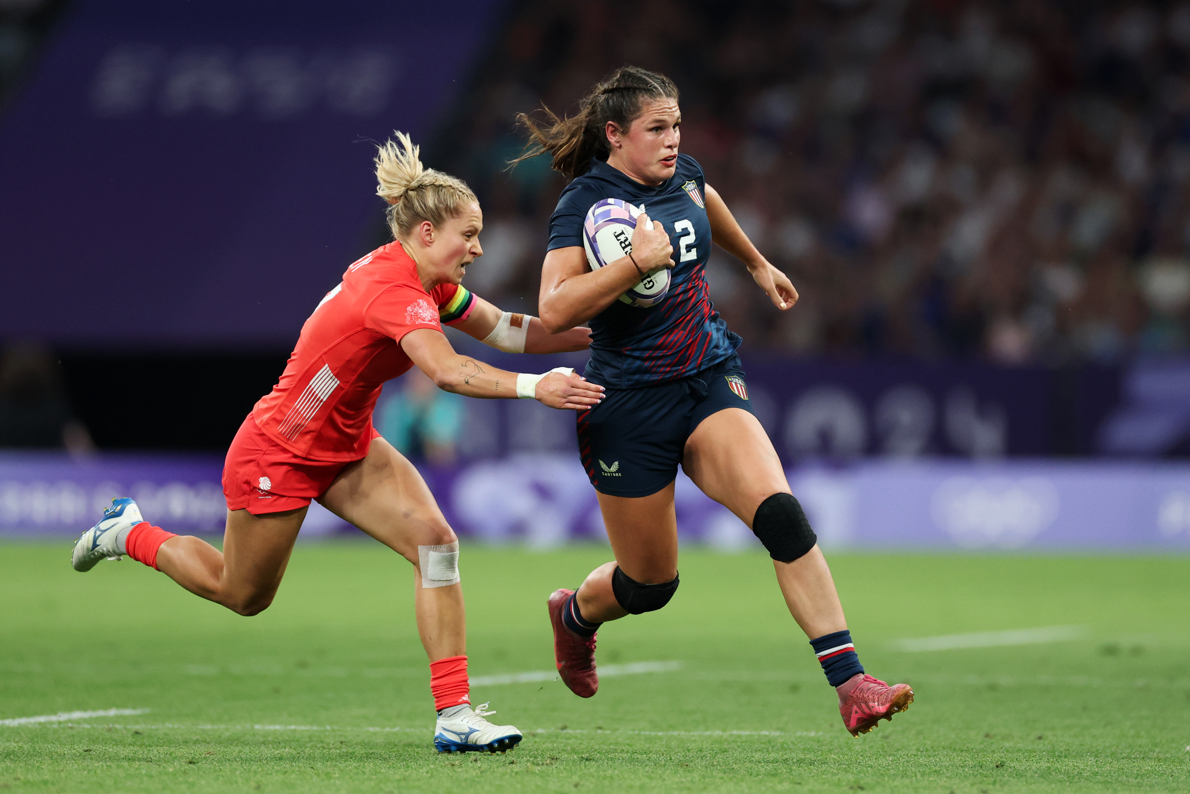 PARIS, FRANCE - JULY 29: Ilona Maher #2 of Team United States runs with the ball whilst under pressure from Emma Uren #7 of Team Great Britain during the Women's Rugby Sevens Quarter Final match between Team Great Britain and Team United States on day three of the Olympic Games Paris 2024 at Stade de France on July 29, 2024 in Paris, France. (Photo by Michael Steele/Getty Images)