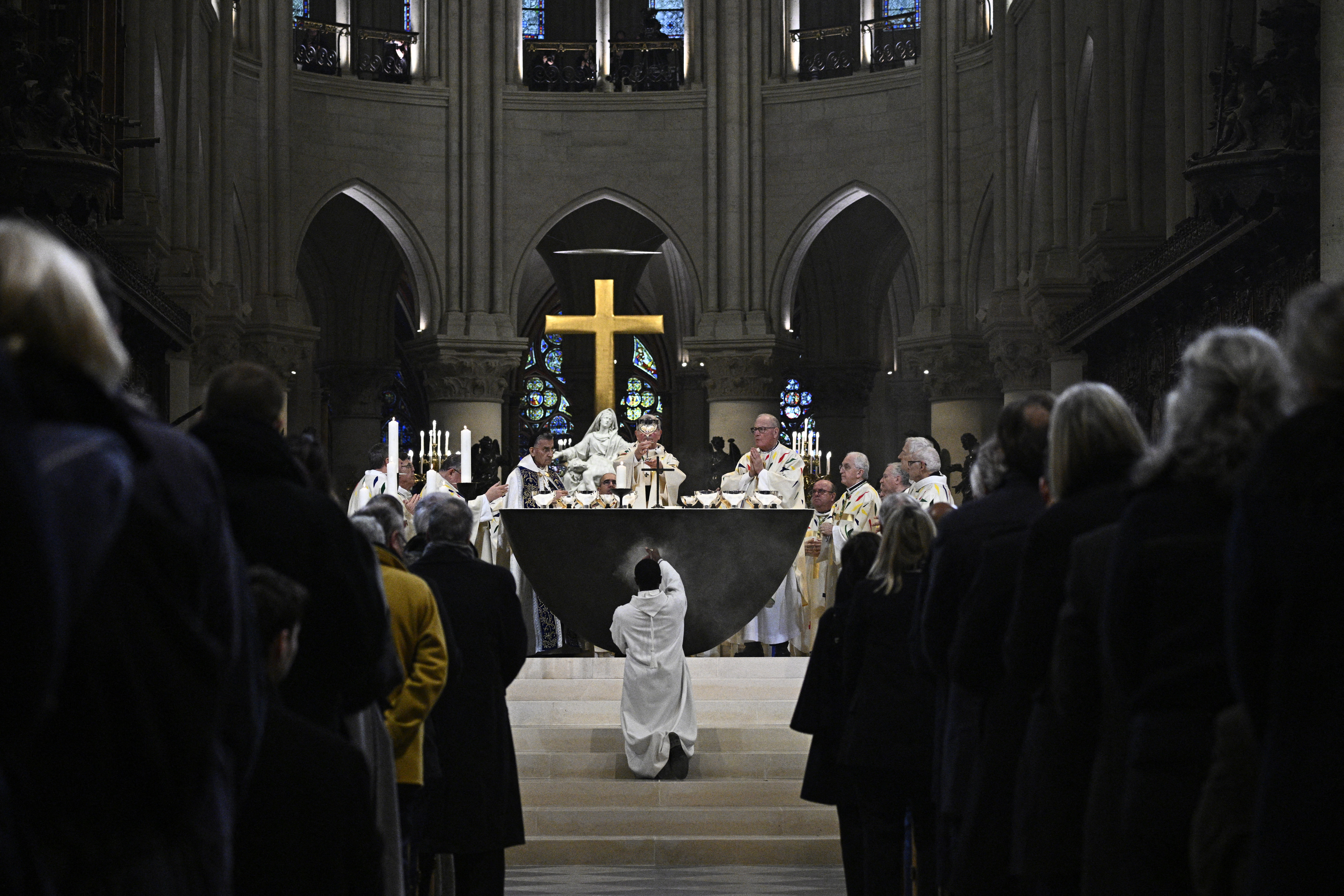 TOPSHOT - A member of the clergy kneels down as the Archbishop of Paris Laurent Ulrich (C) leads prayers for the consecration of the new main altar, designed by French artist and designer Guillaume Bardet which replaces the old one that was destroyed in 2019, during a mass at the Notre-Dame de Paris cathedral, in Paris on December 8, 2024. Newly restored Notre Dame cathedral is set to hold its first service for the public on December 8, 2024 after a historic re-opening ceremony that saw firefighters, builders and artists celebrated for their work saving the 12th-century masterpiece. The beloved Paris monument nearly burned down in 2019, but has been renovated inside and fitted with a new roof and spire during a frenzied reconstruction effort since then. (Photo by JULIEN DE ROSA / AFP) / RESTRICTED TO EDITORIAL USE - MANDATORY MENTION OF THE ARTIST UPON PUBLICATION - TO ILLUSTRATE THE EVENT AS SPECIFIED IN THE CAPTION (Photo by JULIEN DE ROSA/AFP via Getty Images)