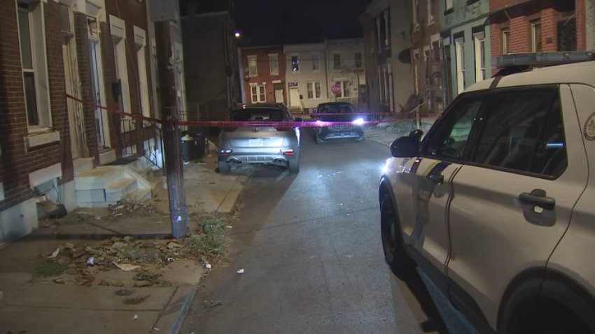 Police car parked in front of police tape at shooting scene.