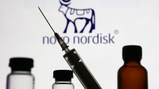 Medical bottles and syringe are seen with Novo Nordisk logo displayed on a screen in the background.