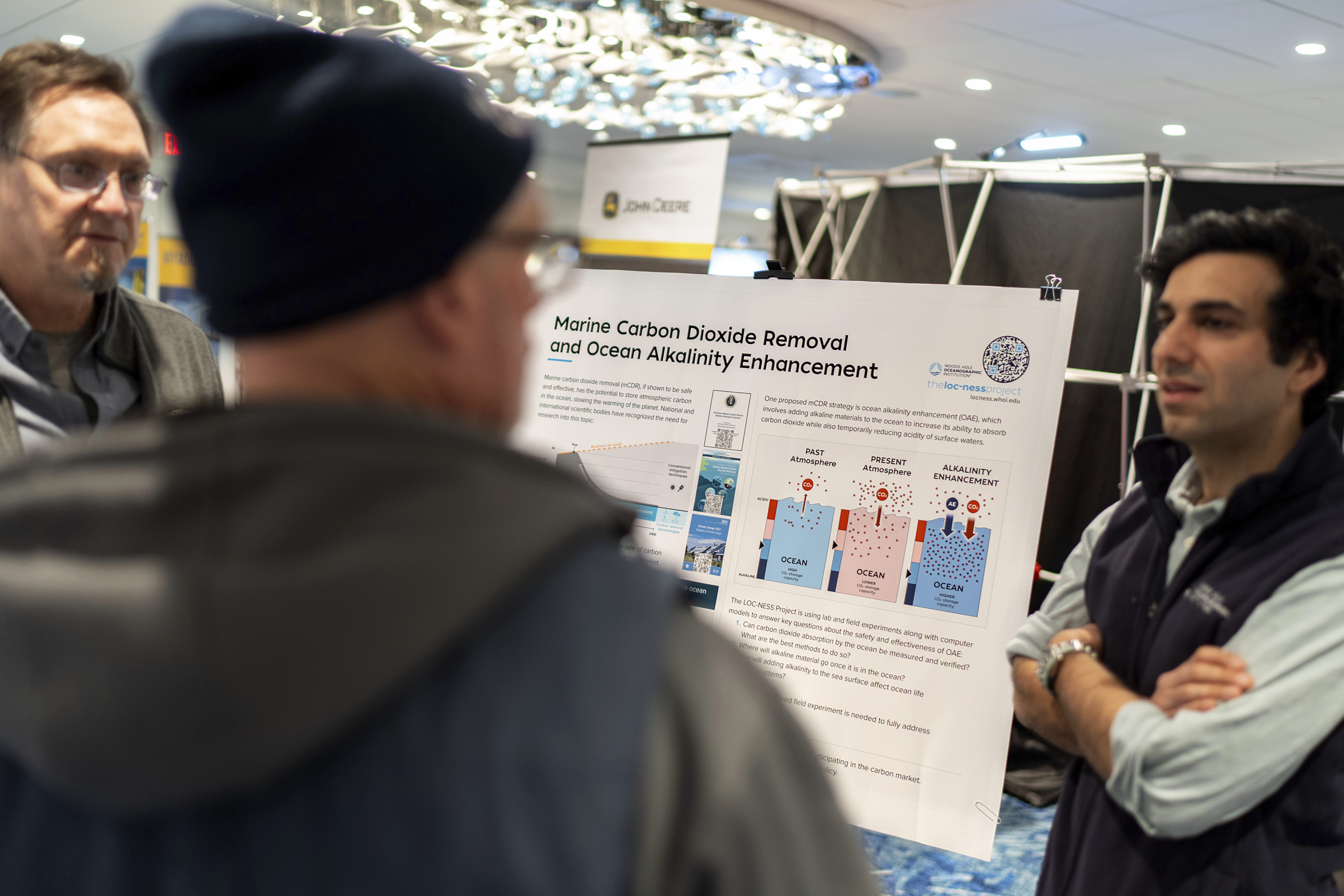An information board is displayed by the Woods Hole Oceanographic Institution to educate the fishing community on an ocean carbon project as scientist Adam Subhas, right, and Ken Koster, left, director of research communication, talk with shell fisherman Alex Brown, at the Massachusetts Lobstermen's Association Annual Weekend and Trade Show, Friday, Jan. 31, 2025, in Hyannis, Mass.