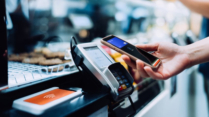 Close up of a woman’s hand paying with her smartphone in a cafe, scan and pay a bill on a card machine making a quick and easy contactless payment. 