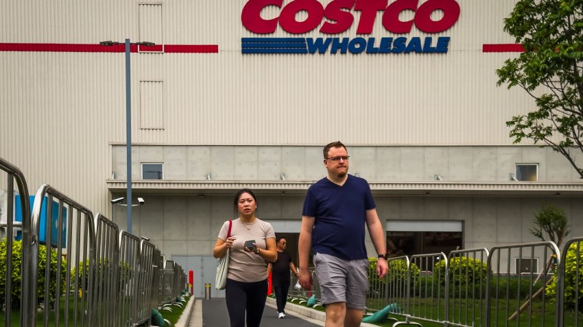 Shoppers walk along a fenced path outside a Costco Wholesale store, with the retailer’s bold red and blue signage visible on the warehouse-style building in the background, on April 12, 2025 in Shenzhen, China.