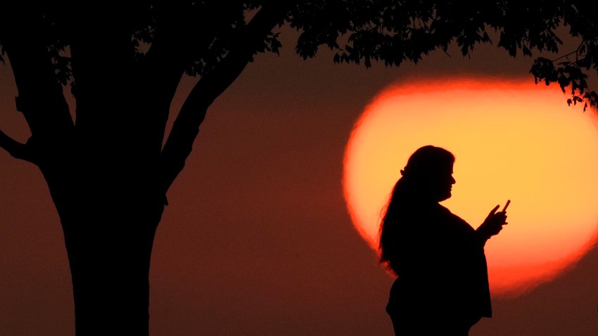 A woman looks at her phone while watching the sun set in Kansas City, Mo.