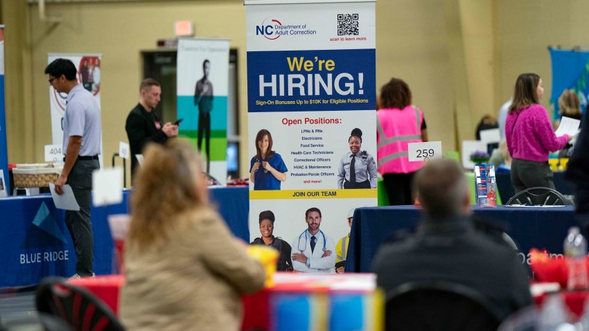 A “We’re Hiring” sign at a NC Department of Adult Correction booth at a job and resource fair hosted by the Asheville Area Chamber of Commerce in partnership with NCWorks in Fletcher, North Carolina, US, on Wednesday, April 9, 2025. 